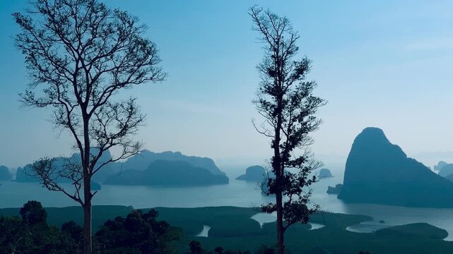 Horizontal video of scenic tree branches silhouette over spectacular sunrise morning sky at Samet Nangshe in Phang Nga, Thailand. Iconic Avatar limestone mountain islands on calm water background. Cli