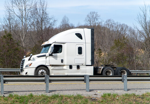 Modern white Freightliner Cascadia semi-truck tractor unit driving on a highway, showcasing essential logistics and transportation for commerce and industry on a clear day.