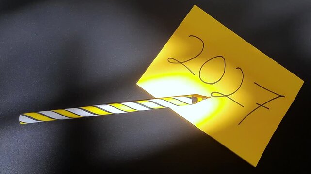 Handwritten 2027 On Yellow Sticky Note With Sunlight Shadow Play and Striped Pen On Dark Background