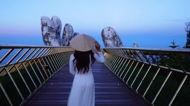 Young tourist girl in white dress walks on Golden Bridge in Ba Na Hills, Danang, Vietnam.