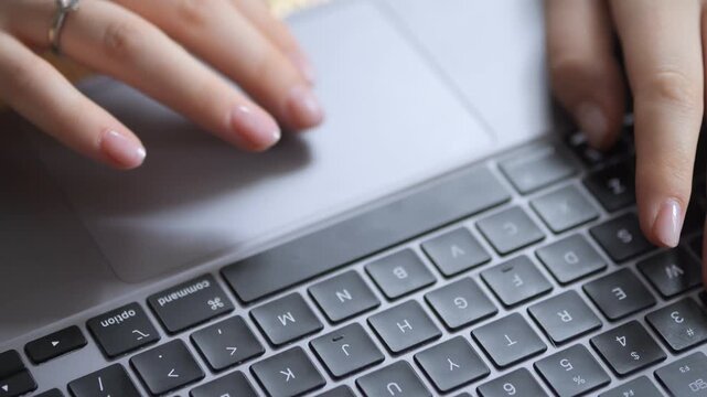 Close-up of hands typing on a laptop keyboard. Fingers press keys with precision. Touchpad area visible above keyboard. Soft lighting highlights skin and laptop surface. No animals or plants shown