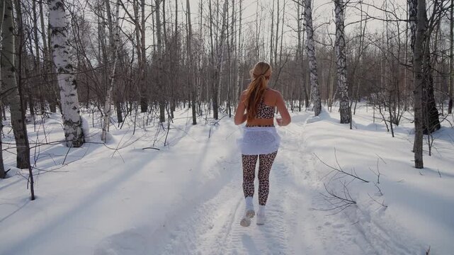 Fitness Woman running winter at forest nature. Fit sportswoman jogging on path in park on snowy winter day. Recreation, snowy weather, winter day.