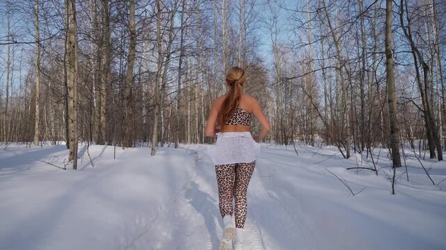 Fitness Woman running winter at forest nature. Fit sportswoman jogging on path in park on snowy winter day. Recreation, snowy weather, winter day.