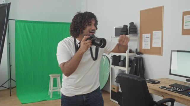 Man holding camera and gesturing to pose in a studio with green screen and reflector, framing a shot; focused creativity.