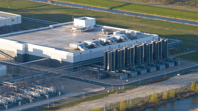 Aerial view of the Google GRQ data center with its industrial cooling systems and modern architecture surrounded by green fields and a canal in Eemshaven, Groningen, Netherlands.