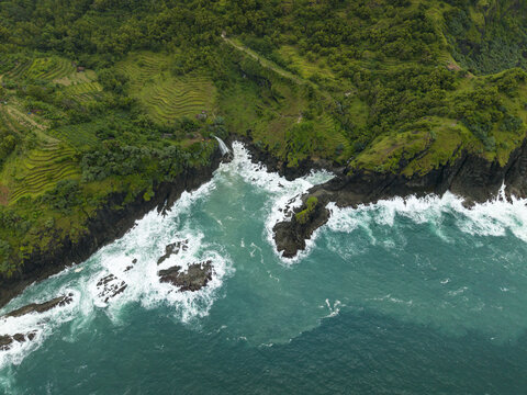 Aerial view of Banyutibo Water Fall cascading from lush green cliffs into the turquoise ocean waves Girisubo, Special Region of Yogyakarta, Indonesia.