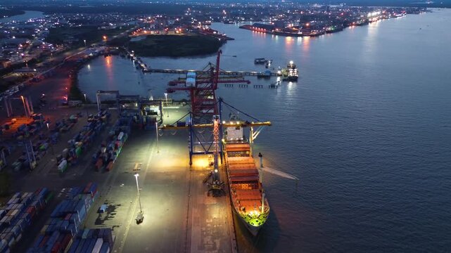 Aerial view of container port with crane loading cargo ship at dusk in busy harbor