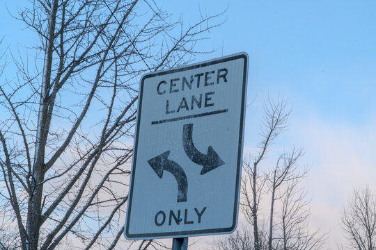 Center Lane Only road sign with explicit directional arrows for turning, set against a crisp winter sky with bare frosted trees, symbolizing traffic rules, guidance, and critical decision-making on