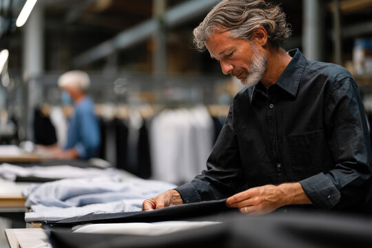 A focused craftsman folds a tailored black garment with precision, highlighting the craftsmanship and meticulous effort put into fashion in an upscale clothing environment.