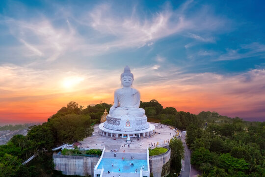 Great white marble Buddha statue sits serenely atop a lush Phuket hill top aerial view sunset sky