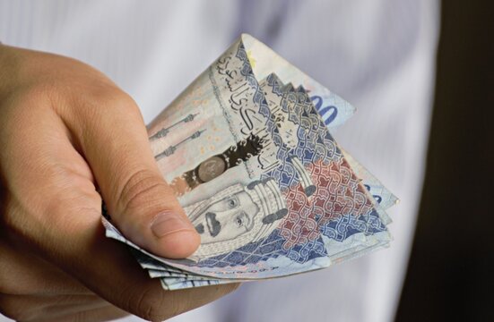 Close-up of a person holding a fan of Saudi Arabian 500 Riyal banknotes, financial and business concept.