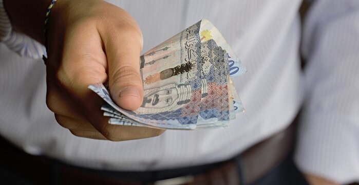 Close-up of a person holding a fan of Saudi Arabian 500 Riyal banknotes, financial and business concept.