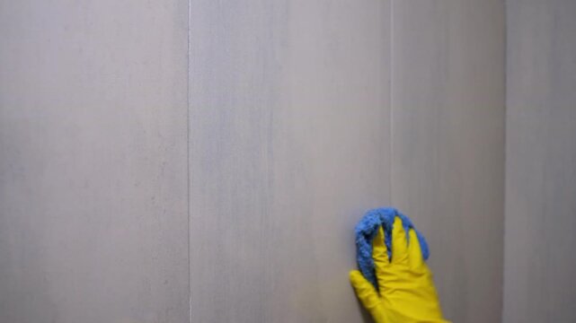 Hand in yellow gloves spraying cleaner on tile surface and wiping. Household cleaning, hygiene and sanitation concept, close-up action. 
