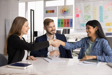 Three professionals take part in negotiations in modern conference room, two women shaking hands,...