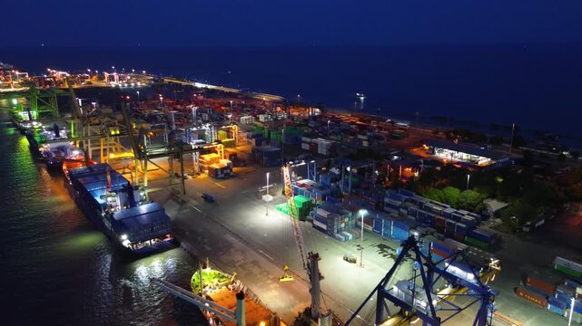Aerial view of container port with crane loading cargo ship at night in busy harbor