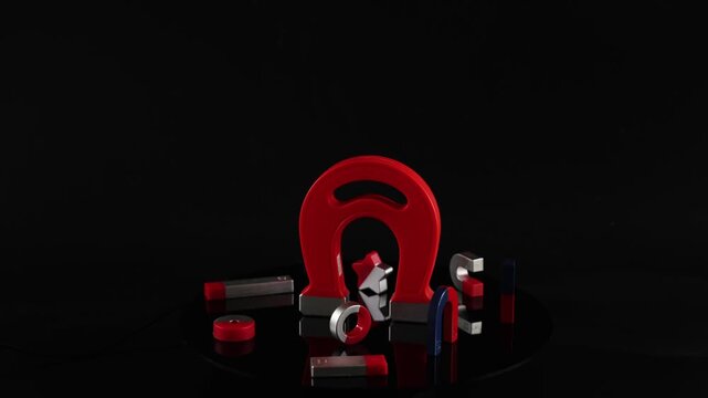 Large red horseshoe magnet rotating with smaller magnetic shapes on black surface.