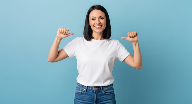 Confident young woman in white t-shirt and jeans pointing at herself with thumbs up studio shot