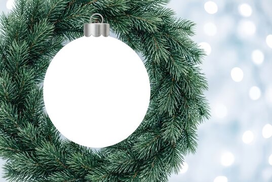 Wreath made of green pine branches with a large white blank circular ornament in the center against a blurred bokeh light background