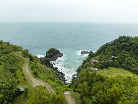 Aerial view of Banyutibo Water Fall meeting the turquoise ocean waves along the lush green cliffs and rocky coastline of Girisubo, Special Region of Yogyakarta, Indonesia.