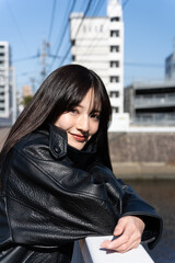 Fototapeta premium 都会の風景をバックに、笑顔で見つめるロングヘアの女性のポートレート