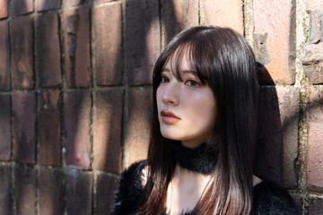 Fototapeta premium レンガの壁を背に、黒いファーニットを着て佇む若い日本人女性のポートレート