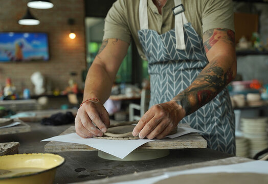 An adult man makes a ceramic plate in a workshop