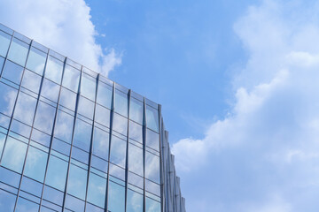 Fototapeta premium Modern glass curtain wall office building reflecting blue sky and clouds with copy space