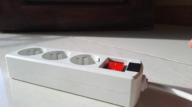 Close-up of an Asian man's hand plugging in and unplugging an extension cord into a power strip. The footage shows switching the power button on and off, connecting an electric cable for charging.