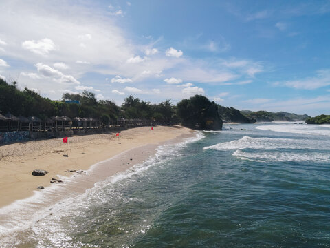 Aerial view of Baron Beach with its sandy shoreline, rolling ocean waves, and traditional huts nestled under green trees Tanjungsari, Special Region of Yogyakarta, Indonesia.