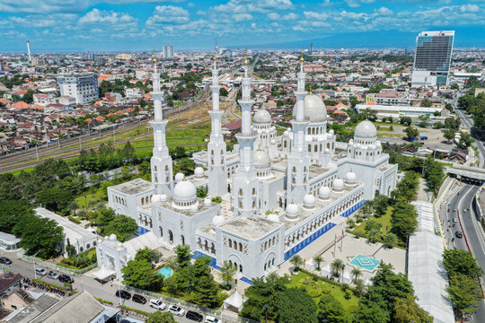Aerial view of Sheikh Zayed Grand Mosque Solo Surakarta with its white domes and tall minarets surrounded by the urban landscape and lush greenery in Kecamatan Banjarsari, Jawa Tengah, Indonesia.