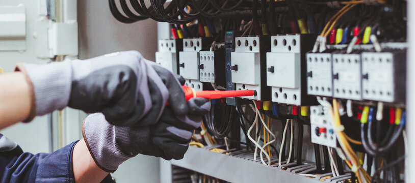 Electrician technician repairing electrical control panel in industrial factory.