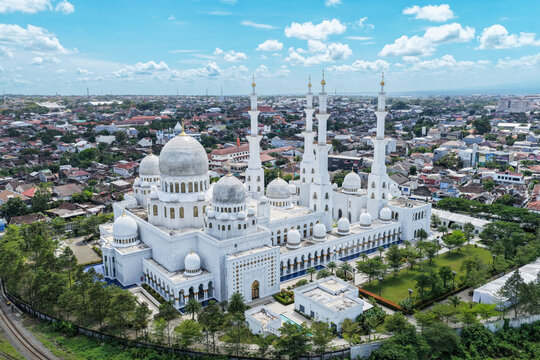 Aerial view of Sheikh Zayed Grand Mosque Solo Surakarta with its white domes and tall minarets surrounded by the urban landscape and green trees in Kecamatan Banjarsari, Jawa Tengah, Indonesia.