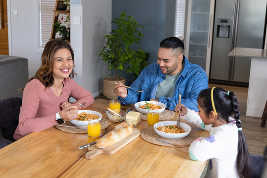Family with mother, father and child sharing pasta at home dining table with bread and juice