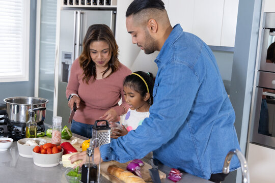 Asian couple and daughter preparing meal on kitchen island with cutting board, box grater, knife