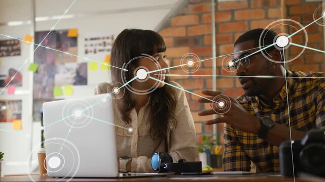 Man gesturing, woman watching laptop, animated nodes expanding across desk for business planning