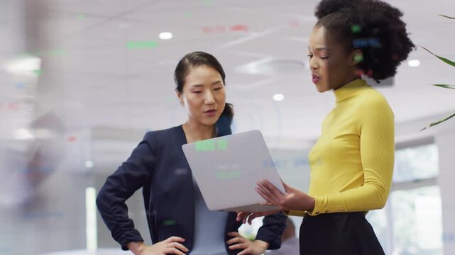 Pair holding laptop, one speaking, other pointing and tapping laptop, green data glass for business