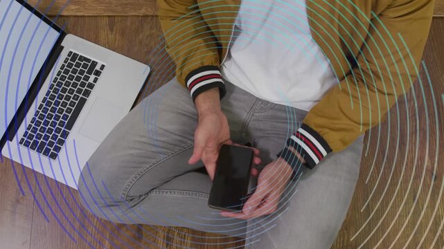 Man adjusting phone, tapping beside laptop, activating rings, settling on right thigh for tech demo