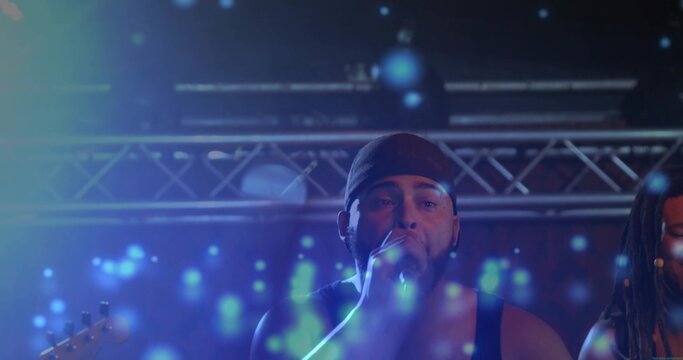 Singing lead vocalist wearing dark bandana, sleeveless top on concert stage, holding handheld mic