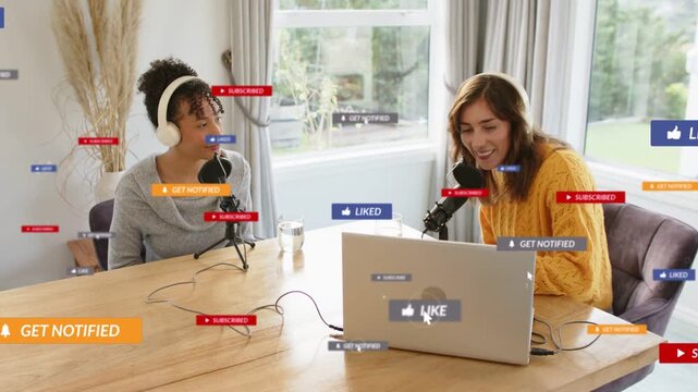 Two female podcast hosts in headsets chatting at wood table, laptop getting live likes showing buzz