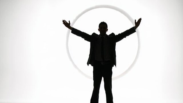 Silhouette of businessman raising arms in triumphant celebration against bright white background