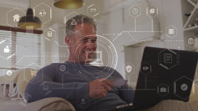 Man sitting in living room chair with card tapping laptop activating finance moneybag icon paying