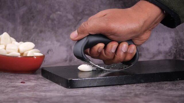 Hand pressing garlic on a cutting board in the kitchen