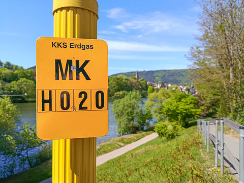 German Sign indicating the location of an underground natural gas line, with a river and a small town in the background