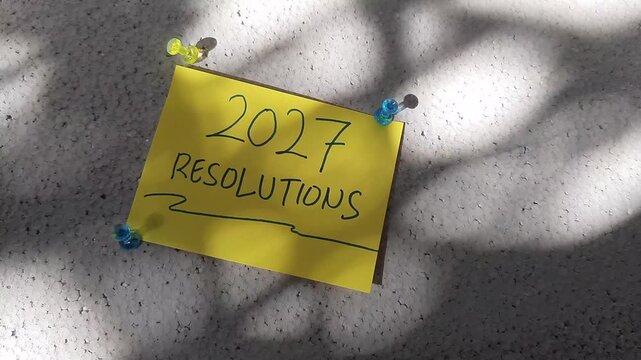 2027 Resolutions Handwritten On Yellow Sticky Note Pinned Under Swaying Sunlight Shadows