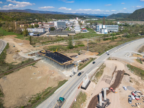 Aerial view of the bridge construction site over a railway line with industrial buildings and green hills in Slovenska Lupca, Banskobystricky kraj, Slovakia.