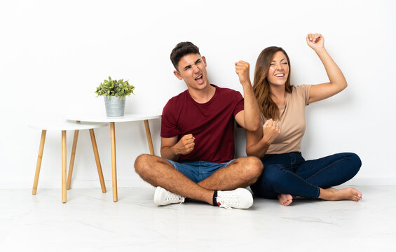 Young couple sitting on the floor isolated on white background celebrating a victory
