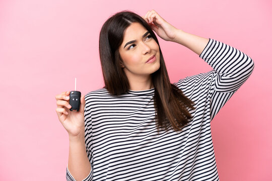 Young Brazilian woman holding car keys isolated on pink background having doubts and with confuse face expression