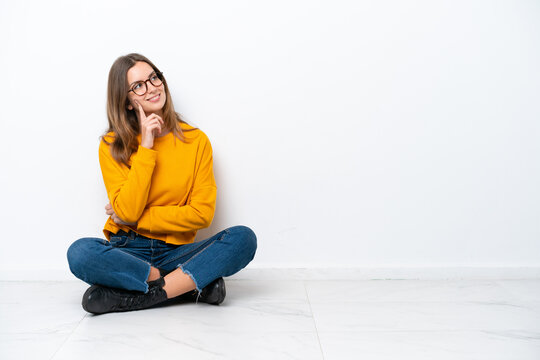 Young caucasian woman sitting on the floor isolated on white background thinking an idea while looking up