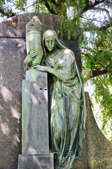 eine Frauenstatue umarmt eine Urne die auf einer Säule steht auf einem Friedhof in Köln © Blende8