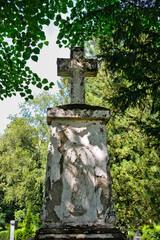 sehr alter Grabstein mit einem Kreuz im Schatten der Bäume auf einem Friedhof in Köln © Blende8